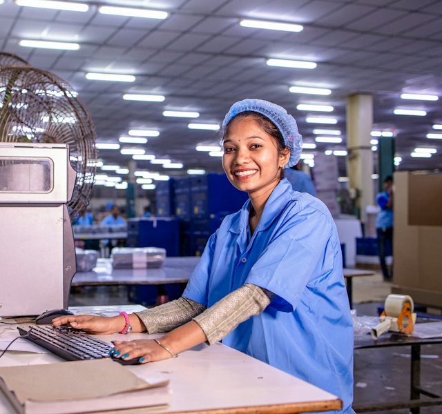 Funcionária sorrindo no computador de uma fábrica