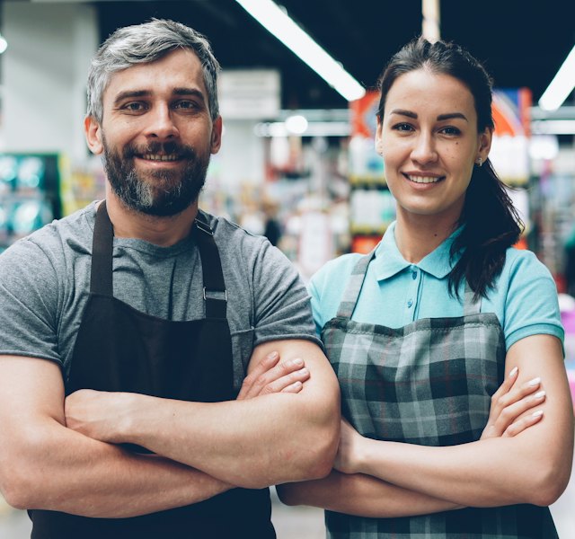Dois funcionários de um mercado sorrindo de braços cruzados